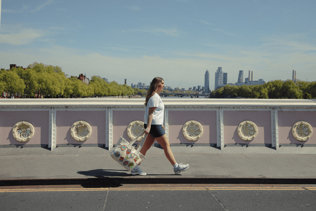 Woman walking with a colorful tote on a bridge with a city skyline in the background