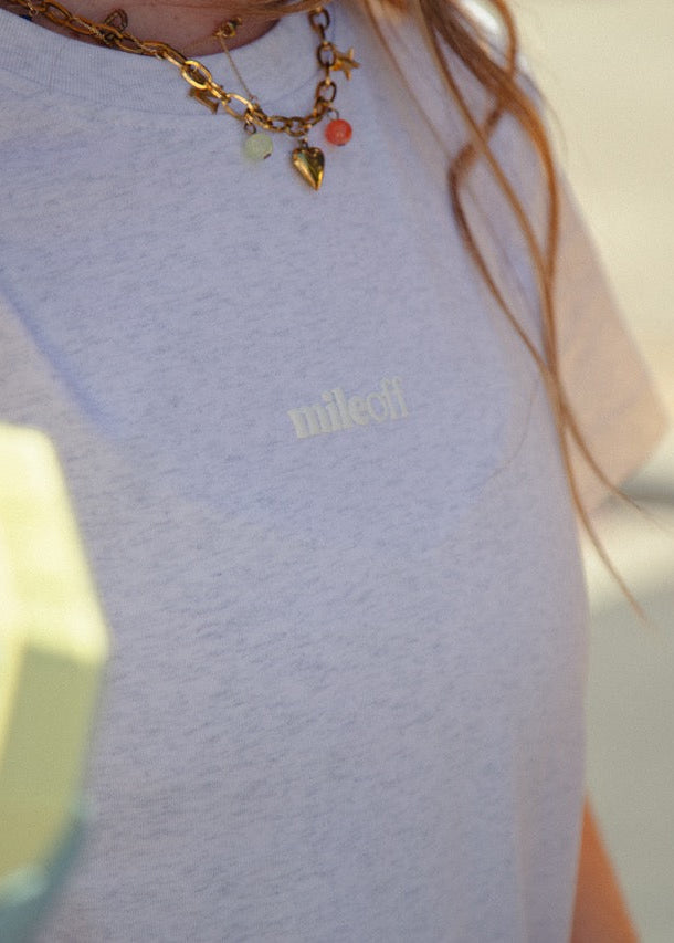 Person wearing a light grey sweatshirt with 'mileoff' logo, holding a green and yellow object.