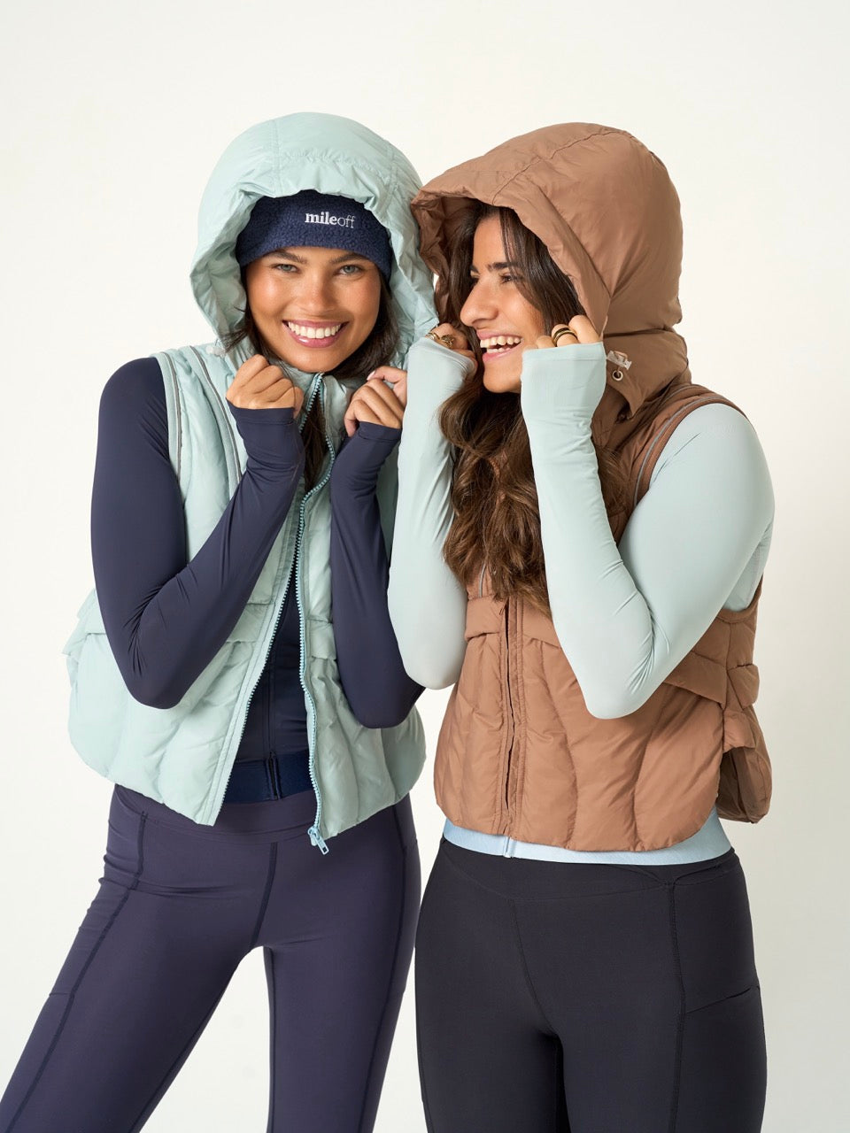Two women wearing hooded vests on a white background